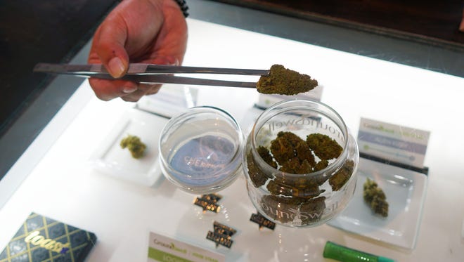 Budtender Tyler Schneckenberger shows off marijuana from a glass jar he was stocking in preparation for increasing sales during the Super Bowl weekend at the GroundSwell cannabis dispensary in Denver.