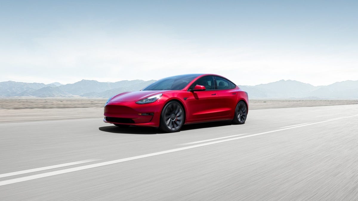 A red Tesla Model 3 traveling on a highway.