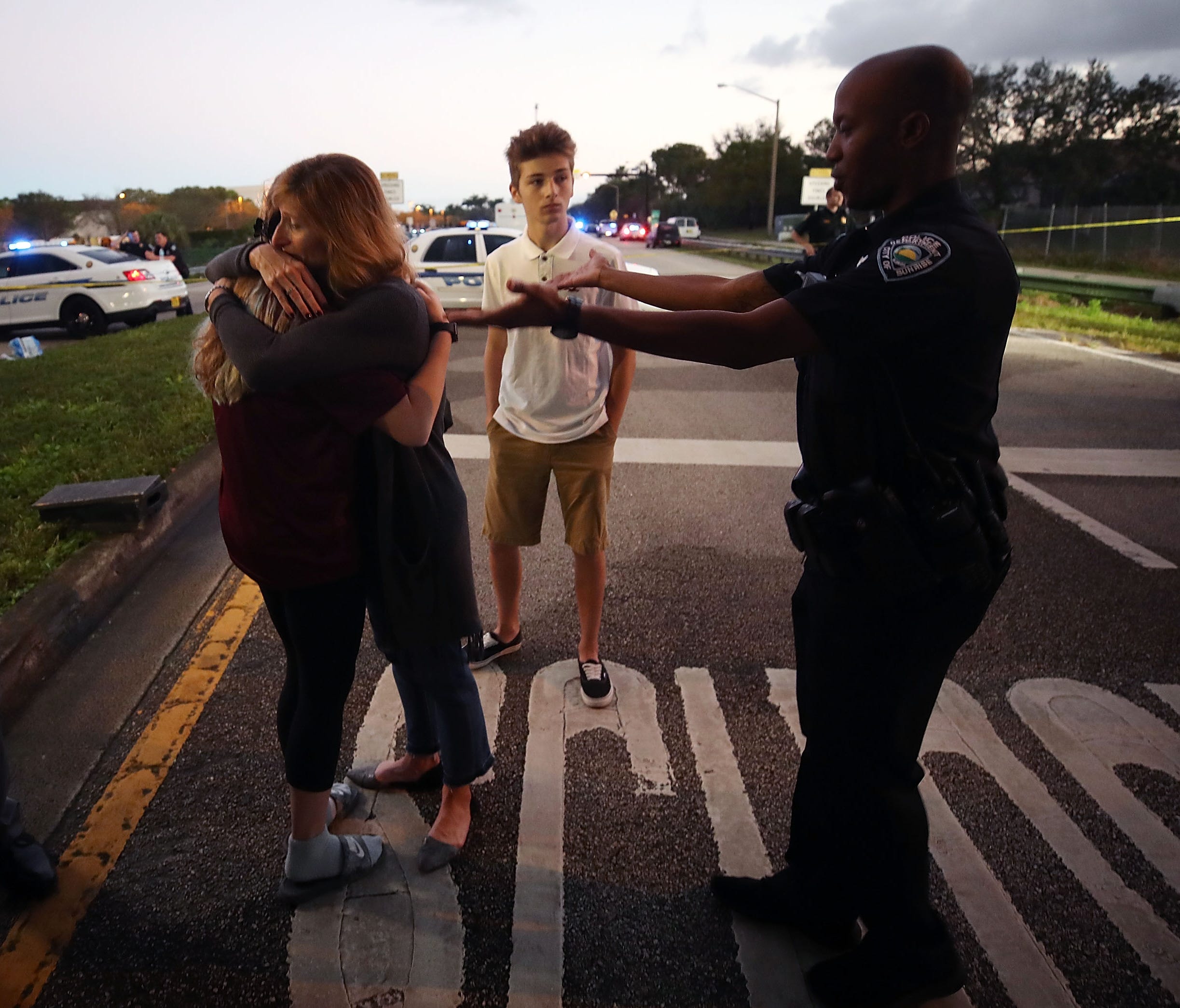 Kristi Gilroy hugs a young woman as a police officer tries to clear a closed road at a police checkpoint near Marjory Stoneman Douglas High School where 17 people were killed by a gunman Feb. 15, 2018, in Parkland, Fla.  Police arrested the suspect a