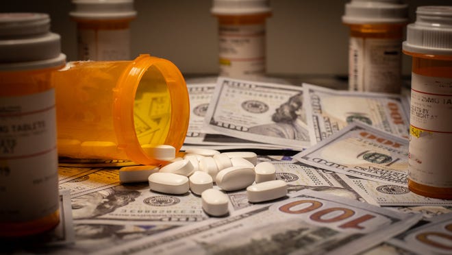 Prescription drugs falling out of a bottle onto cash, with other prescription bottles making a circle around the money.