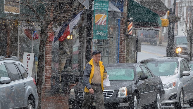 On the first day of spring, a pedestrian crosses North Walnut Street in Milford Friday morning in the snow.