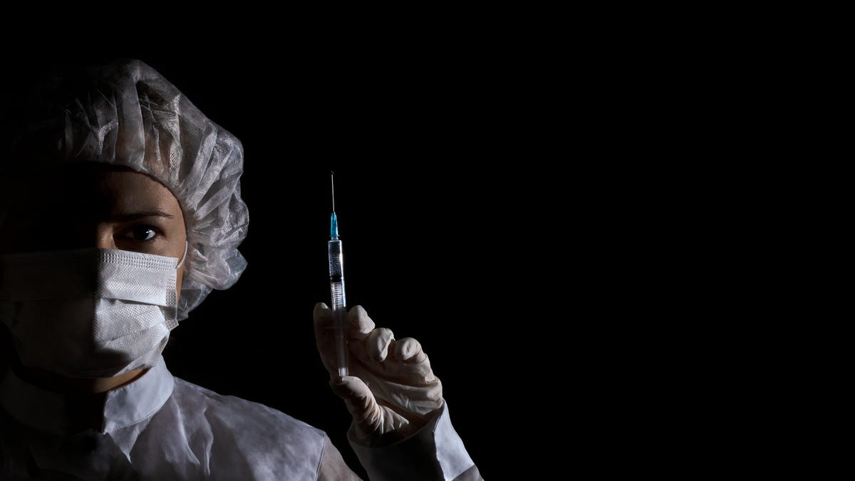 Healthcare professional wearing a mask and holding a vaccine shot