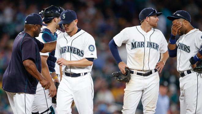 Seattle Mariners pitcher Rob Rasmussen, third from right, walks to the dugout after being relieved for by manager Lloyd McClendon, left, during the eleventh inning of a baseball game Saturday, Aug. 8, 2015, in Seattle. Mariners shortstop Brad Miller, second from right, and second baseman Robinson Cano, right, stand on the mound.