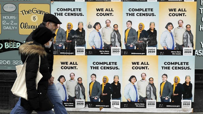 People walk past posters encouraging participation in the 2020 Census, Wednesday, April 1, 2020, in Seattle's Capitol Hill neighborhood.