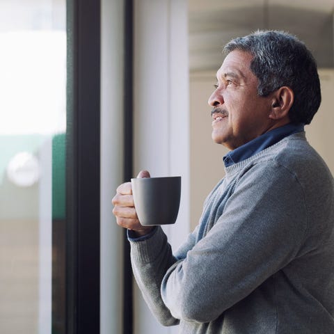 Older person holding a mug and looking out a windo