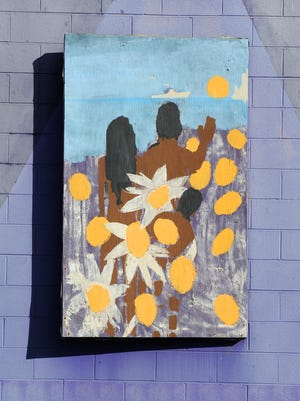 On the left panel, which was painted first, a family waves hello, or goodbye, at a passing ship, their backs simply depicted in strong browns and bold yellows, the color of daisies and the sun.