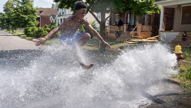 Michael Greer of Detroit jumps over water flowing from an open hydrant on Townsend Street in Detroit's Islandview neighborhood on Tuesday, July 7, 2020 as the family cools off from the heat wave in the running water.
