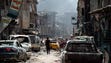 A man walks by destroyed vehicles in a street in the