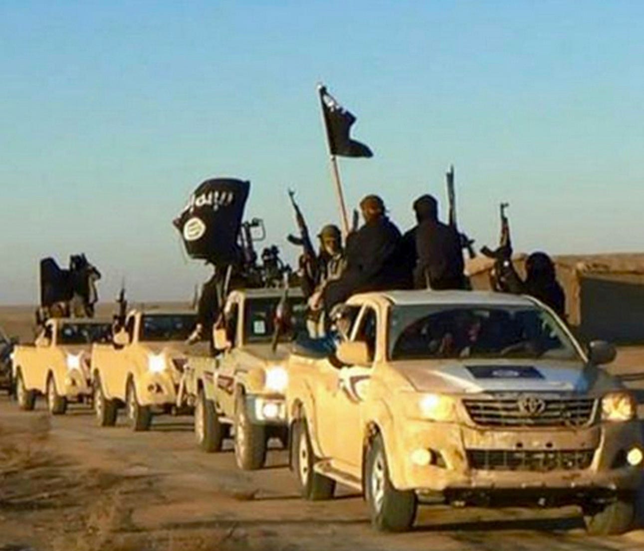 In this undated file photo released by a militant website, which has been verified and is consistent with other AP reporting, militants of the Islamic State group hold up their weapons and wave its flags on their vehicles in a convoy to Iraq, in Raqq
