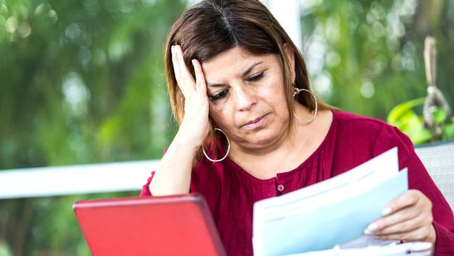 A woman is sitting at the dining table using her tablet to sort her household bills online.She is looking glum as she struggles to sort finances.