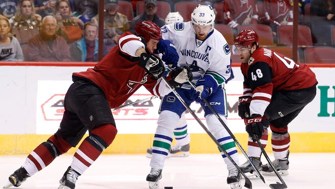 Vancouver Canucks' Henrik Sedin (33), of Sweden, tries to get the puck past Arizona Coyotes' Nicklas Grossmann, left, of Sweden, and Jordan Martinook (48) during the first period of an NHL hockey game Friday, Oct. 30, 2015, in Glendale, Ariz.