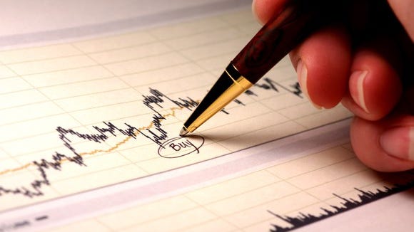 A person's hand writing the word buy underneath a dip on a paper stock chart.