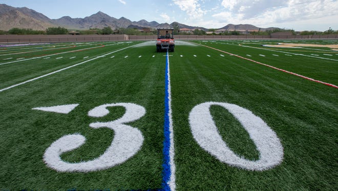 Workers add a thin layer of material to the new football field at Scottsdale Notre Dame Preparatory High School, on Monday, Aug. 18, 2014.