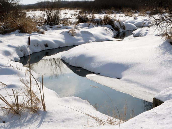 A creek meanders through mounds of snow covered grass