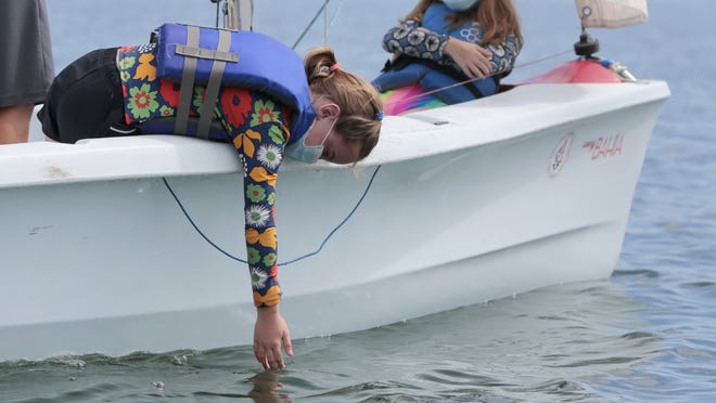 Thalia Leibowitz  runs her hand over the water as her boat sails out into Clark's Cove in the south end of New Bedford as part of the Community Boating Center's  Summer Your Sailing Program.