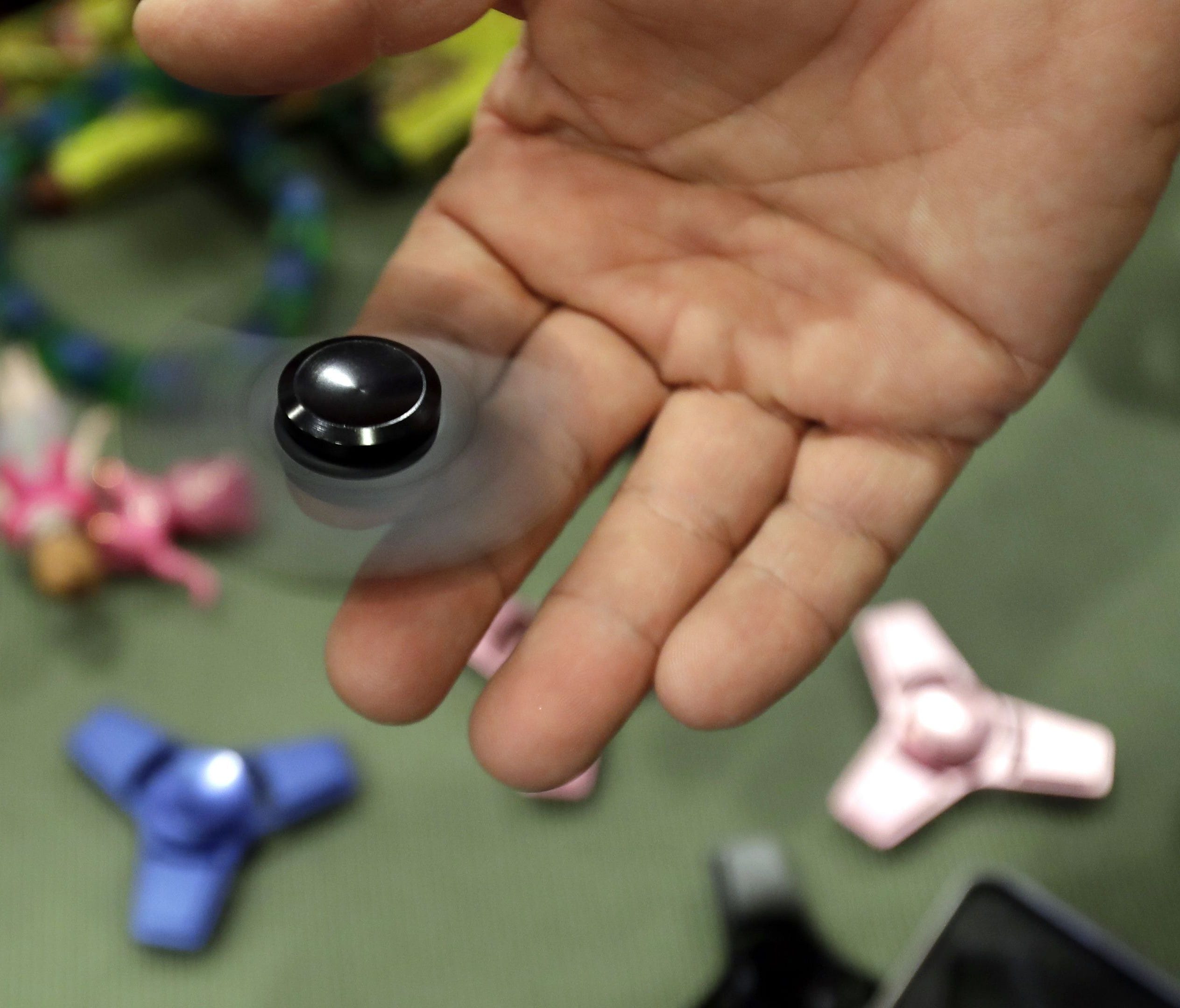 In this Thursday, May 11, 2017, photo, Funky Monkey Toys store owner Tom Jones plays with a fidget spinner in Oxford, Mich. The mania for fidget spinners, the 3-inch twirling gadgets taking over classrooms and cubicles, is unlike many other toy craze