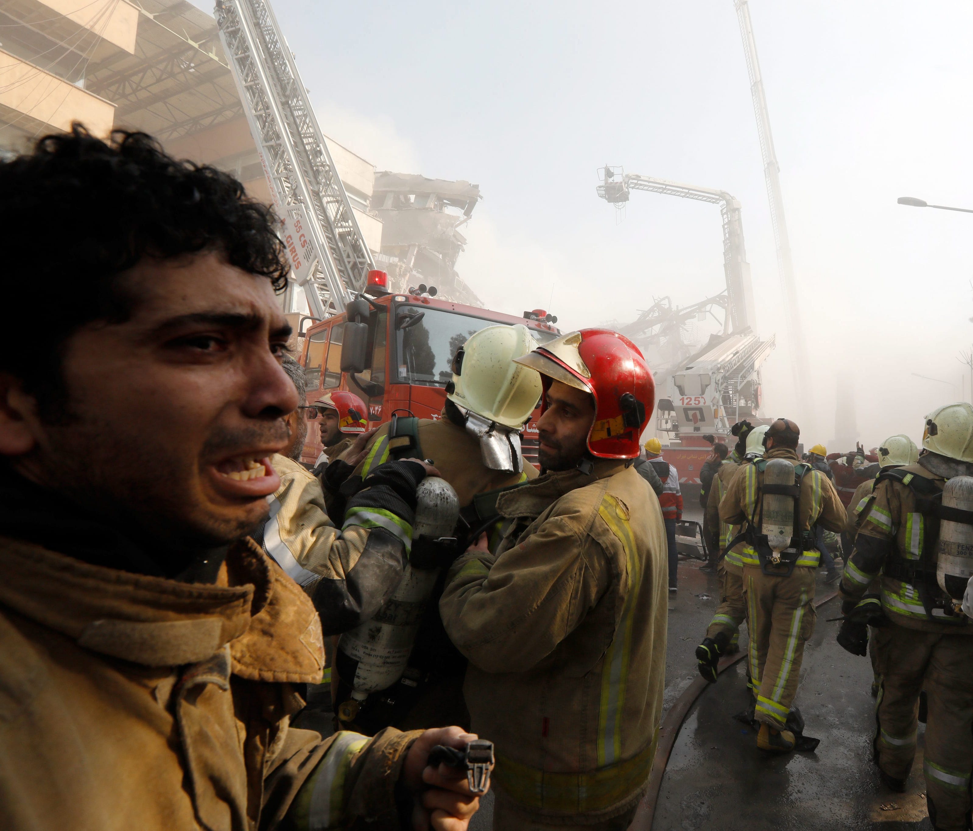 An Iranian fire fighter cry as other prepare as the iconic Plasco building collapses after a fire in Tehran, Iran, Jan. 19, 2017.