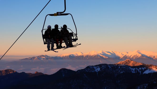 Chair ski lift with skiers over blue sky in the evening.
