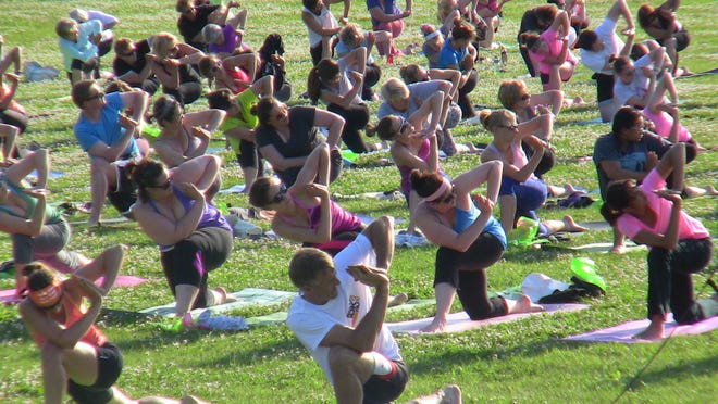 
Members of Ryanne Cunningham’s free yoga class perform a stretch Thursday evening at Voyageur Park off Cass St. in downtown De Pere. More than 200 people showed up for the first class of the year. 
