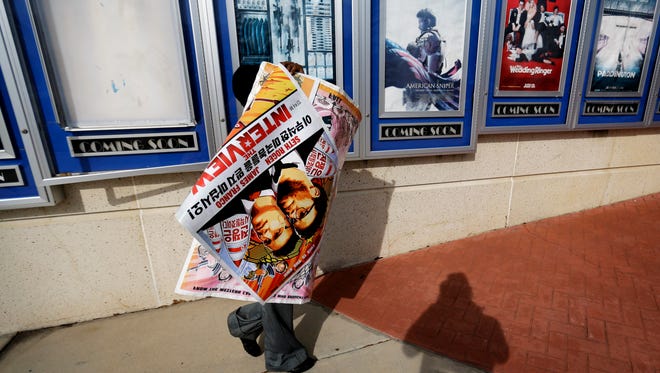 A poster for the movie "The Interview" is carried away by a worker after being pulled from a display case at a Carmike Cinemas movie theater in Atlanta.