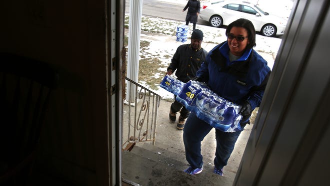 In this January photo, Marseille Allen, 36 of Flint carries up another 40 bottle case of bottled water into the home of brothers James and Jimmie Thompson of Flint.