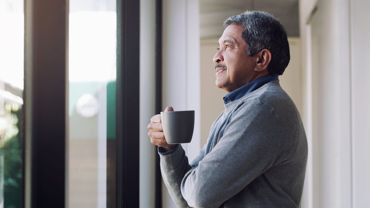 Older person holding a mug and looking out a window.