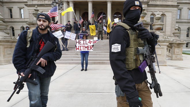 Protesters carry rifles near the steps of the Michigan State Capitol building in Lansing, Mich., on April 15. Flag-waving, honking protesters drove past the Michigan Capitol to show their displeasure with Gov. Gretchen Whitmer's orders to keep people at home and businesses locked during the new coronavirus COVID-19 outbreak.