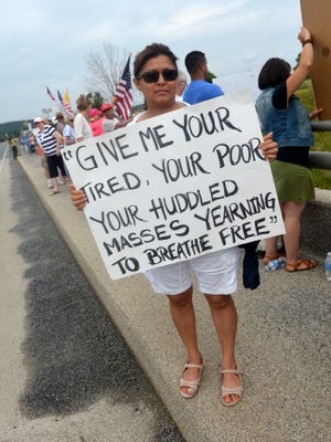 Amparo Zaldivar of Harrisonburg holds a poster for passing motorists to read. They join about 50 people came to the Va. 612 overpass in Verona on Saturday morning, July 19, 2014. They gather to demonstrate for and against various immigration issues, drawn by news that an Augusta County center hosts several undocumented children.