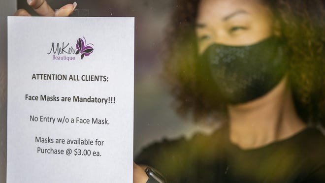 MeKer Beautique co-owner Meshell Pak tapes a sign in the North Austin salon's window Thursday after Mayor Steve Adler issued a new order requiring face coverings in all Austin businesses.