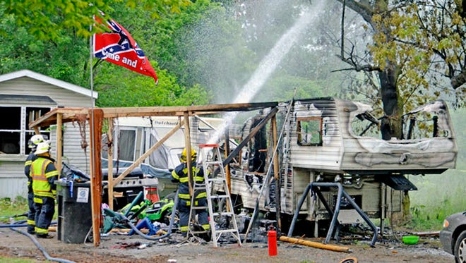 In this Monday, June 11, 2018, photo, Bronson firefighters wet down a smoldering tree at the scene of a fatal fire in Bronson, Mich. Authorities say there's no indication of foul play in the camper fire in southern Michigan that killed two young siblings and a dog and injured a third child.