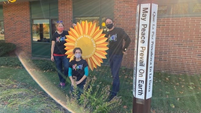 Jessica Wilke, music teacher; Kate Blehar, art; and Michael Walsh, physical education, at the giant sunflower next to the Houghton Elementary peace pole.