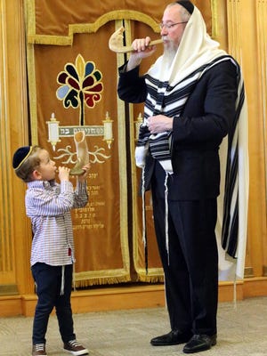 Rabbi Yisrael Greenberg shows his 3-year-old grandson Menachem Greenberg how to blow the shofar, a trumpet used in Jewish religious ceremonies. Greenberg wears a Tallit, a shawl worn during morning prayer and on Jewish holidays.
