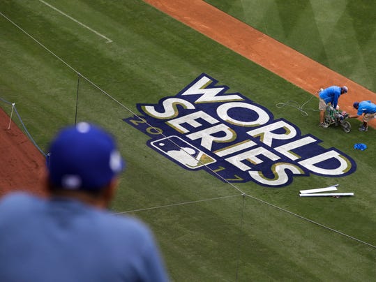 A fan watches as workers paint the World Series baseball logo on the field at Dodger Stadium ahead of Tuesday's Game 6 of baseball's World Series between the Los Angeles Dodgers and the Houston Astros, Monday, Oct. 30, 2017, in Los Angeles. (AP Photo/Jae C. Hong)
