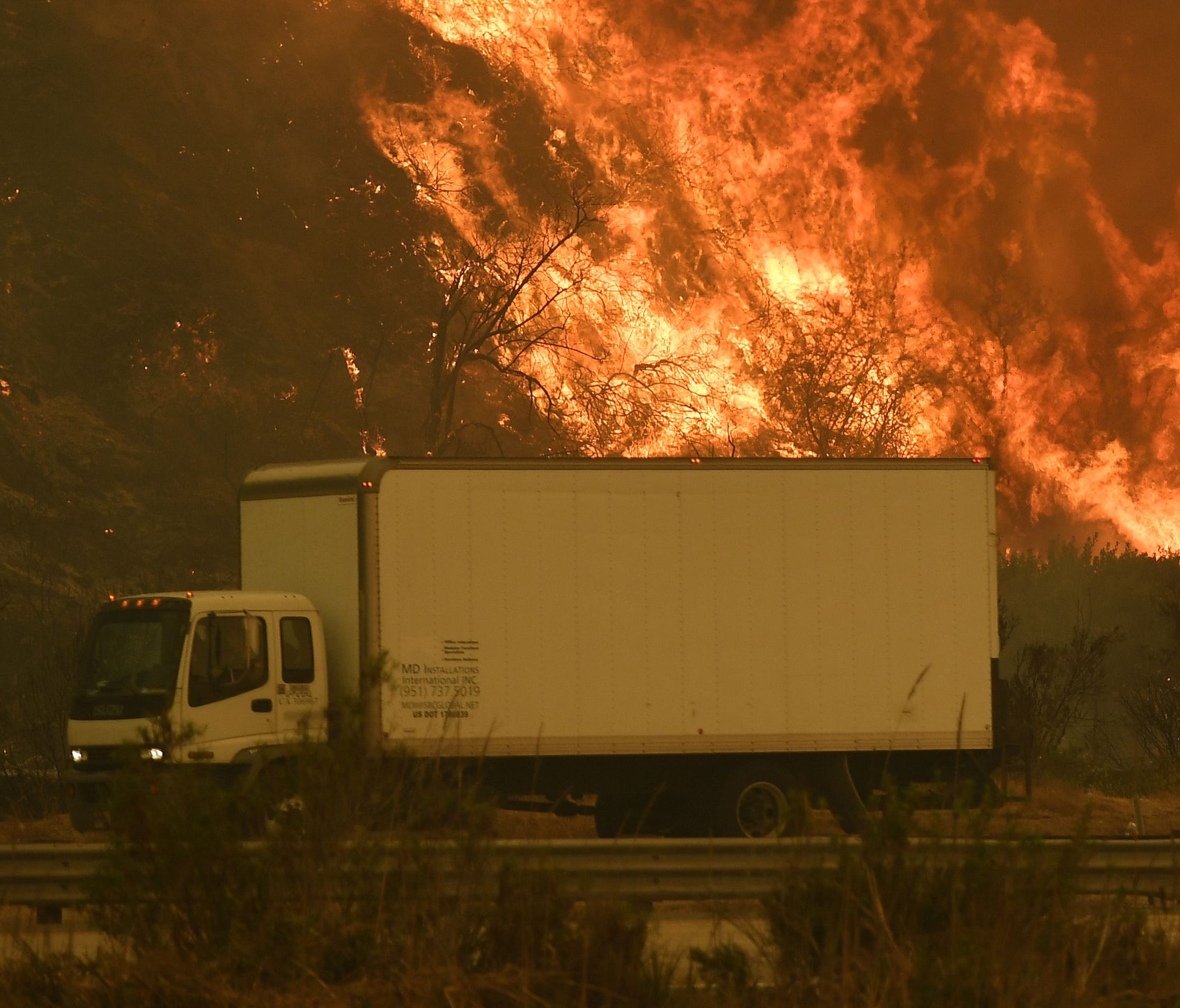Vehicles pass beside a wall of flames on the 101 highway as it reaches the coast during the Thomas wildfire near Ventura, Calif., on Wednesday.
