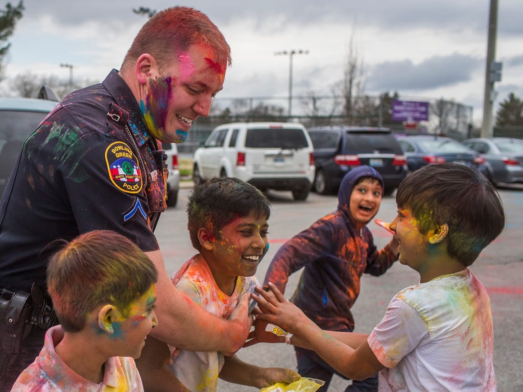 Bowling Green Police Officer Drew Bittel smiles as children surround him during a Holi festival celebration at Kereiakes Park in Bowling Green, Ky.