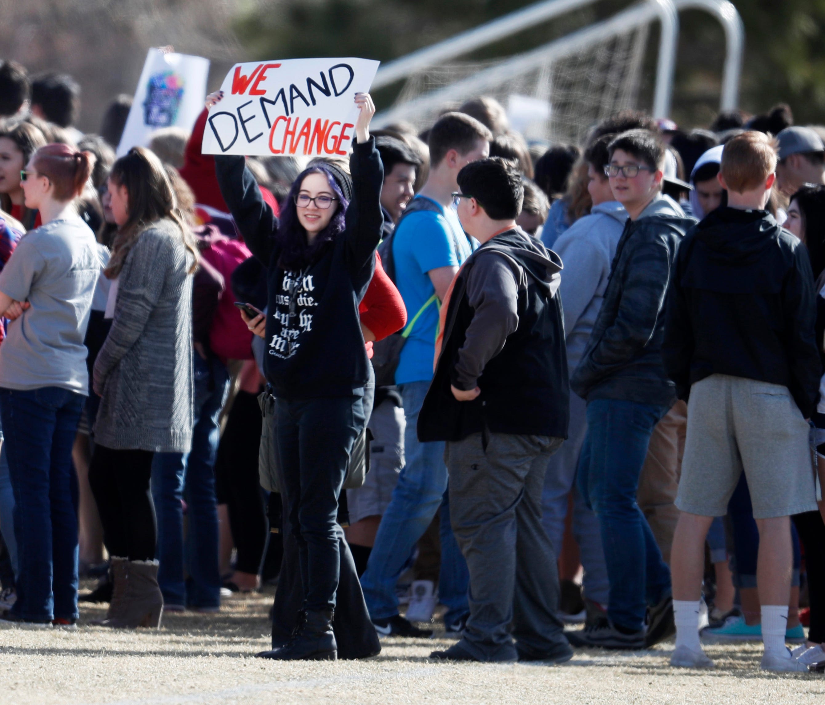 A student waves a sign as classmates gather during a student walkout to protest gun violence on the soccer field behind Columbine High School in Littleton, Colo.