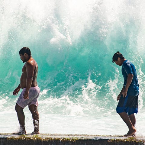 People walk in front of the high surf near Kapahul
