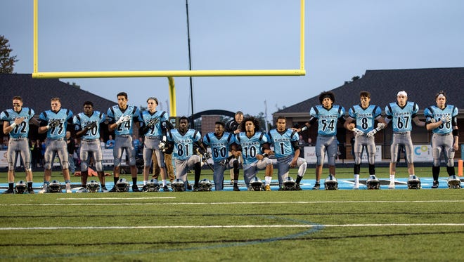 Center from left, Lansing Catholic's Kabbash Richards, Roje Williams, Michael Lynn III and Matthew Abdullah, kneel while the rest of the team stands during the national anthem before the start of the Cougars' game against Ionia on Friday, Oct. 6, 2017, at Cougar Stadium in Lansing. The four players did not start in the game.