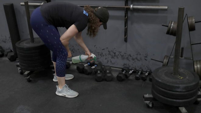 Alexis Garrod, CrossFit Potrero Hill partner and head coach, cleans off weight training equipment after instructing a class over Zoom in an empty gym, which closed for shelter in place orders over COVID-19 concerns, in San Francisco, Friday, April 24, 2020.