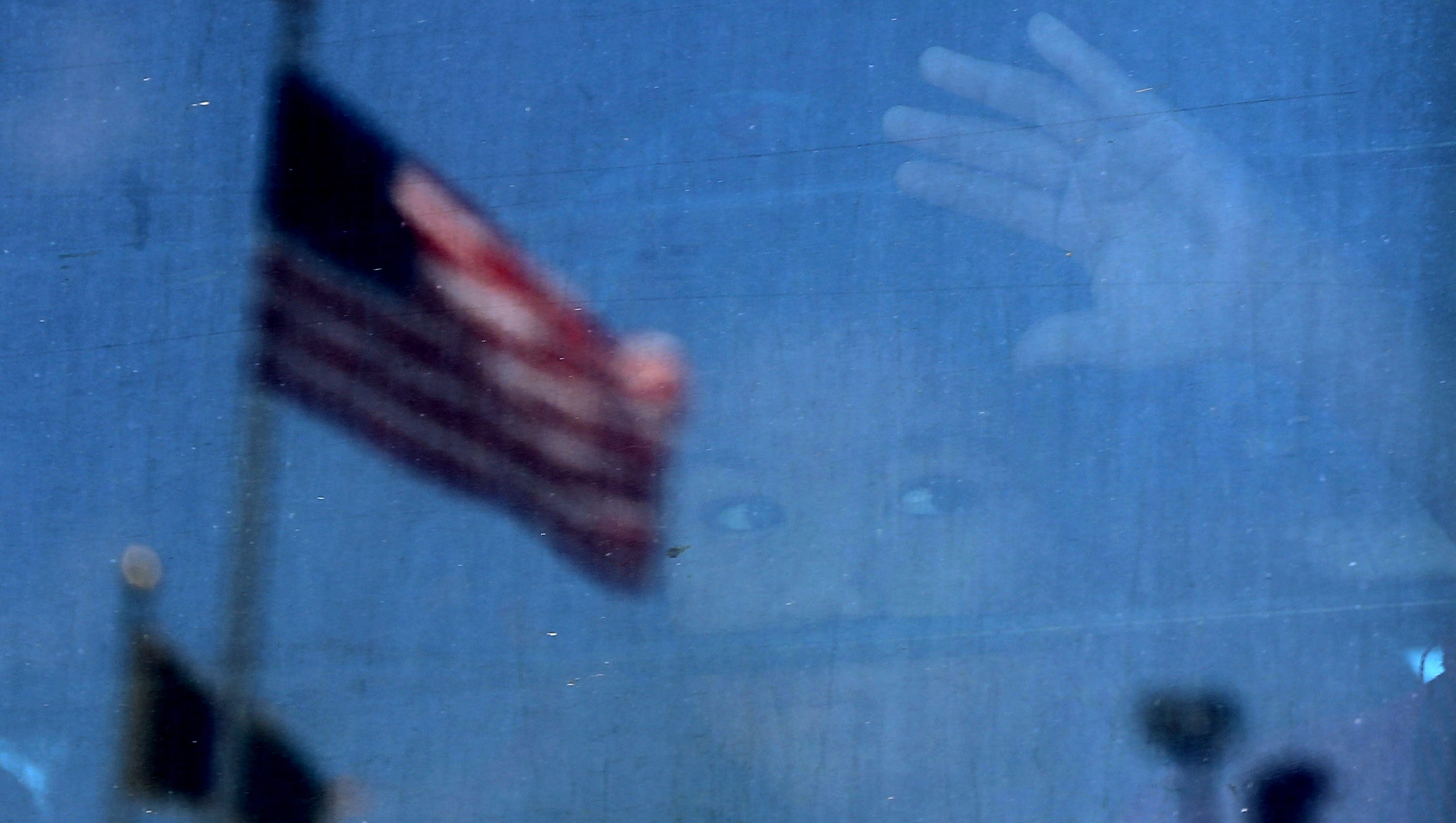 A migrant child looks out the window of a bus as protesters