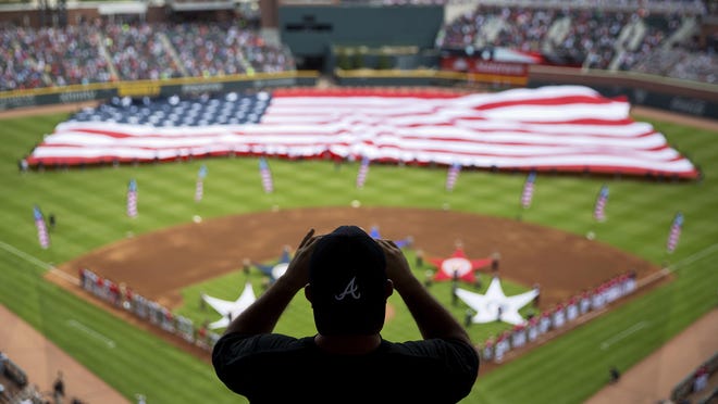 FILE - In this May 20, 2017, file photo, a spectator takes a photo of a United States flag as it is unveiled for the national anthem as part of Military Appreciation Day before a baseball game between the Atlanta Braves and the Washington Nationals in Atlanta. The anthem has been a standard part of U.S. sports games since World War II. Experts say Game 1 of the 1918 World Series between the Boston Red Sox and the Chicago Cubs helped pave the way. The song became the official national anthem in 1931. (AP Photo/David Goldman, File)