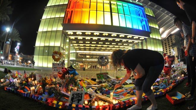 A small crowd gathers on the lawn in front of the rainbow-colored Dr. Phillips Center for the Arts in Orlando late Monday night for a candlelight vigil.