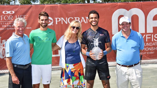 Juan Benitez, 2018 Mardy Fish Children's Foundation tennis tournament champion, holds up the trophy as Fish, right, takes part in post-match festivities.
