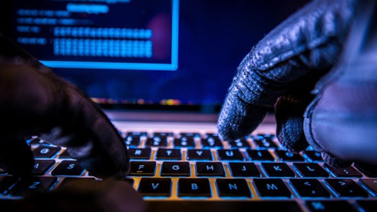 A cybercriminal wearing black gloves and hacking into a computer.