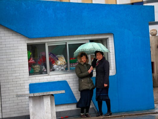 Women shelter from the rain under an umbrella in front