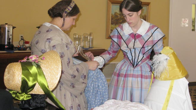 L to r: Malinda Byrne and Megan Barrell, of the Genesee Country Museum, wear period costumes while preparing a display of dresses and accessories.