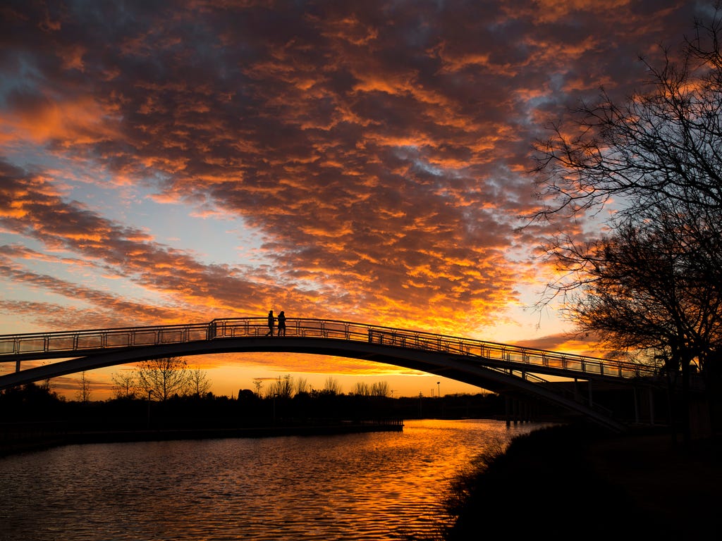 A couple cross a bridge as the sun sets at the King Juan Carlos public park in Madrid, Spain.