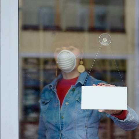 Woman in mask turns store window sign around.