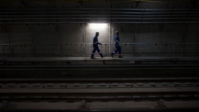 In this June 8, 2016 photo, workers walk in the new underground subway tunnel below Ipanema neighborhood in Rio de Janeiro, Brazil. Two construction workers chatted while applying white grout to the walls of a new subway tunnel one recent day, their voices and the smells of the building materials stark reminders of what was missing: passengers and trains.