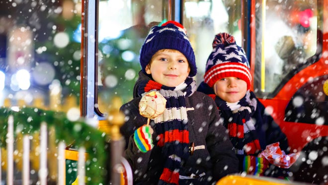 Two little kids boys on a carousel at Christmas funfair or market, outdoors. Happy children having fun and eating sweets. Traditional xmas market in Germany, Europe. Holiday, lifestyle concept.